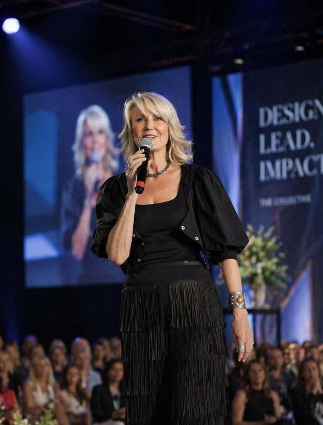 Ros Banksia-Smith on stage holding a microphone, speaking to an audience beneath a Design. Lead. Impact. banner