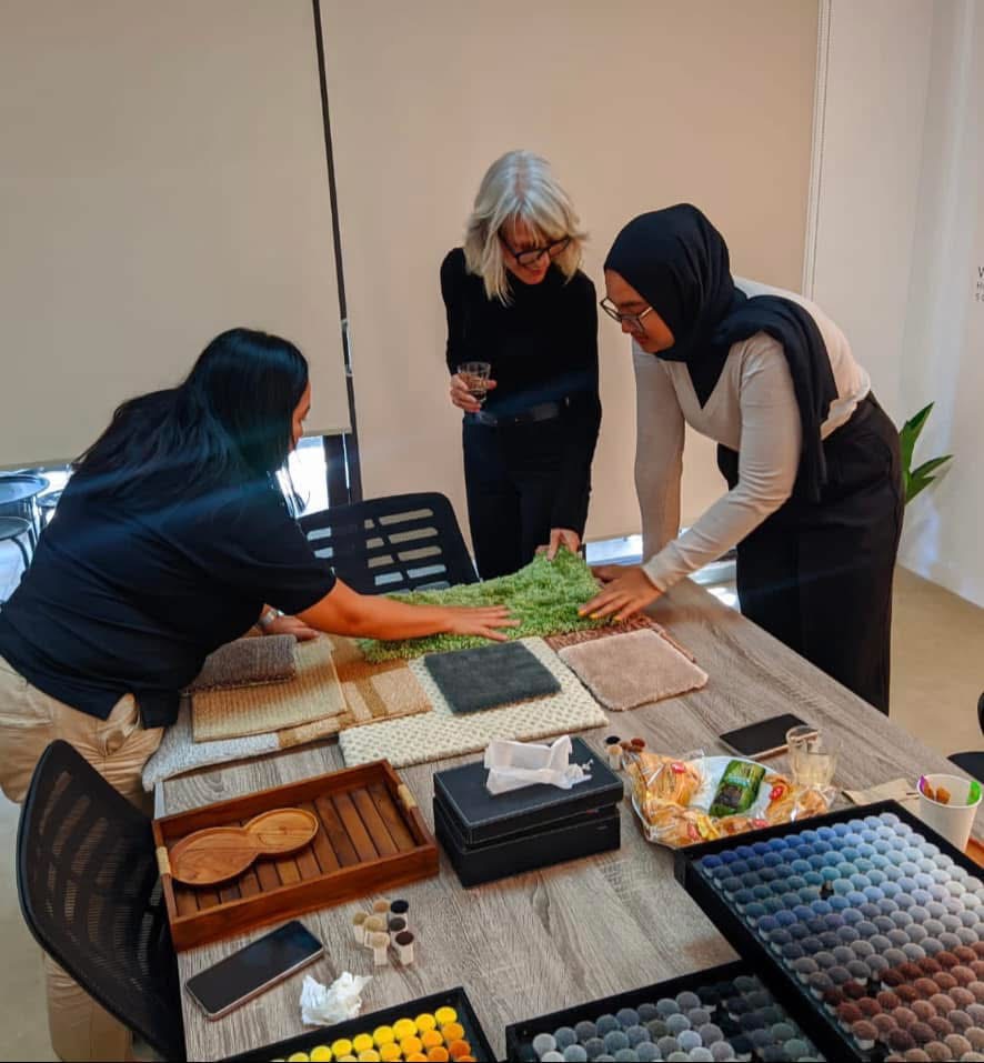 Ros Banksia-Smith reviewing carpet, textile and colour samples at a table with two colleagues
